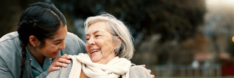 Caregiver helping woman with disability in park for support, trust and care in retirement. Nurse talking to happy senior patient in wheelchair for rehabilitation, therapy and conversation in garden